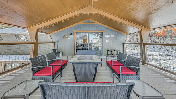 Une terrasse extérieure couverte, dotée d’un plafond en bois, d’une table centrale entourée de chaises et offrant une vue sur les environs.