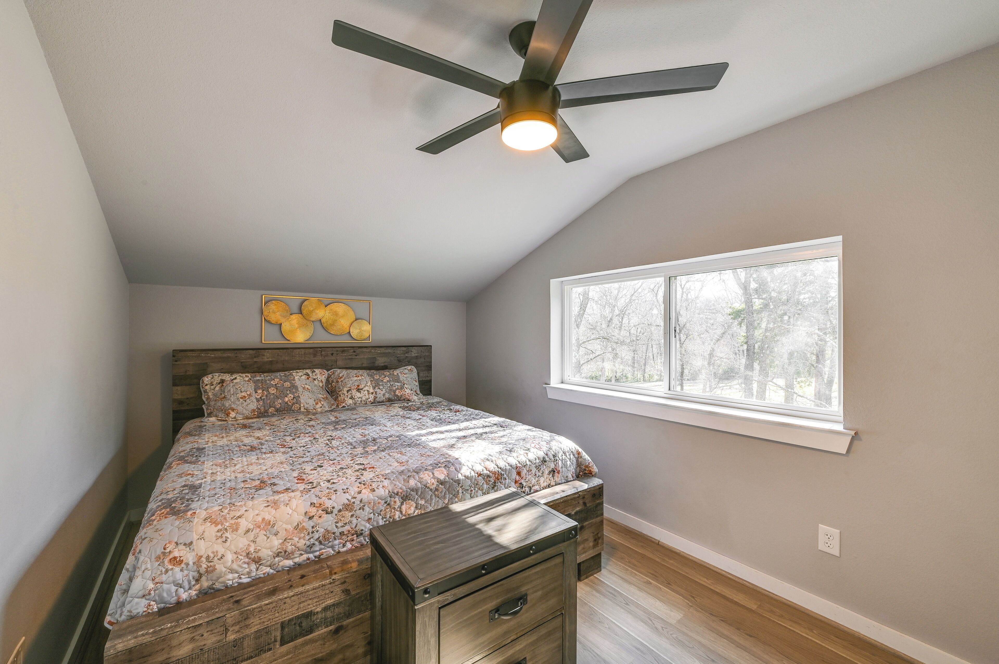 A bedroom with a bed, a ceiling fan, a window, and a nightstand.