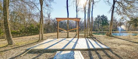 A wooden pergola structure in a park with a paved walkway leading to it.