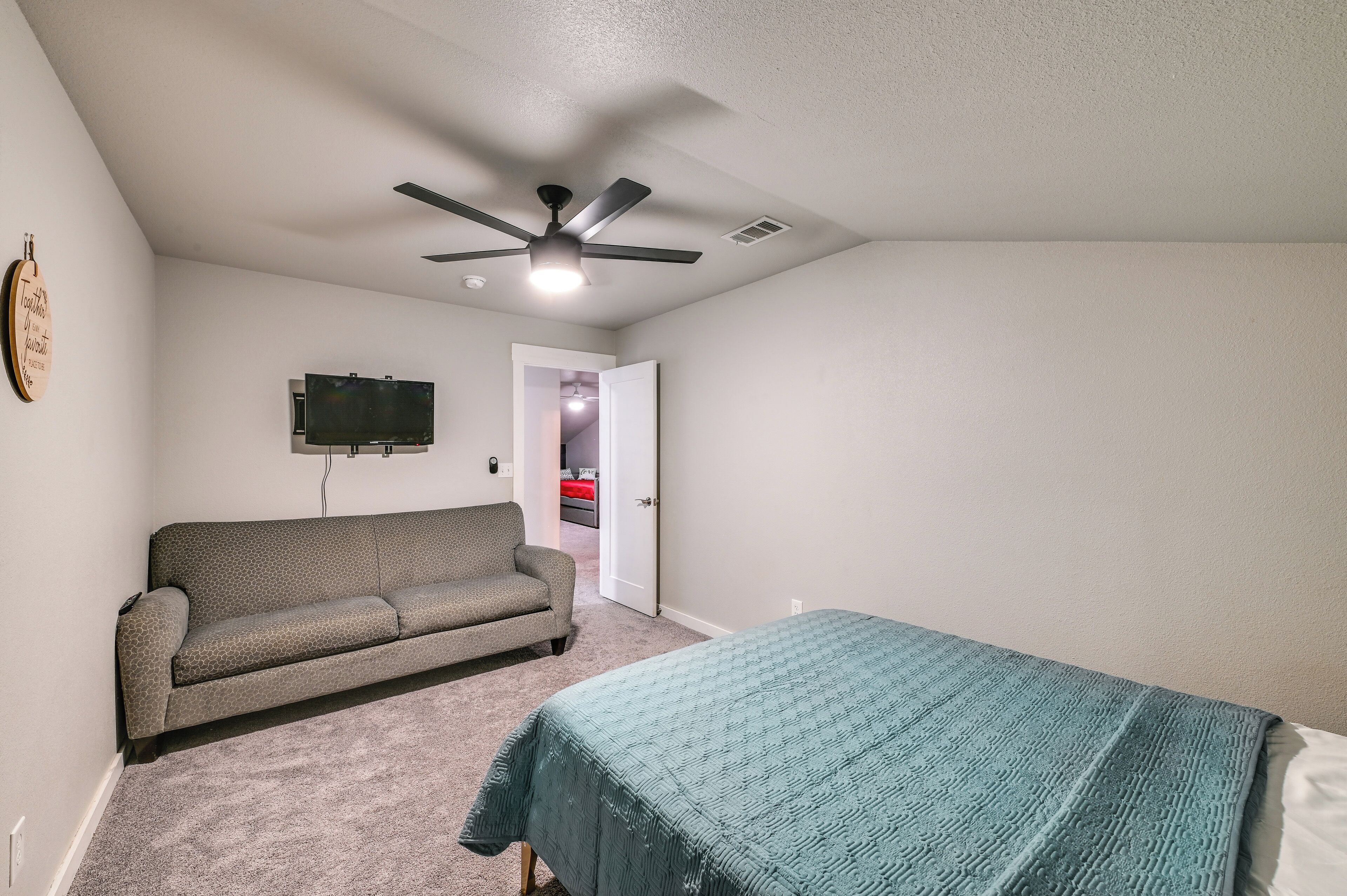 A bedroom with a bed, a sofa, a ceiling fan, and a TV on the wall.