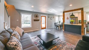A spacious living room with a sofa, coffee table, and patterned rug. A dining area with chairs and a table is visible in the background.