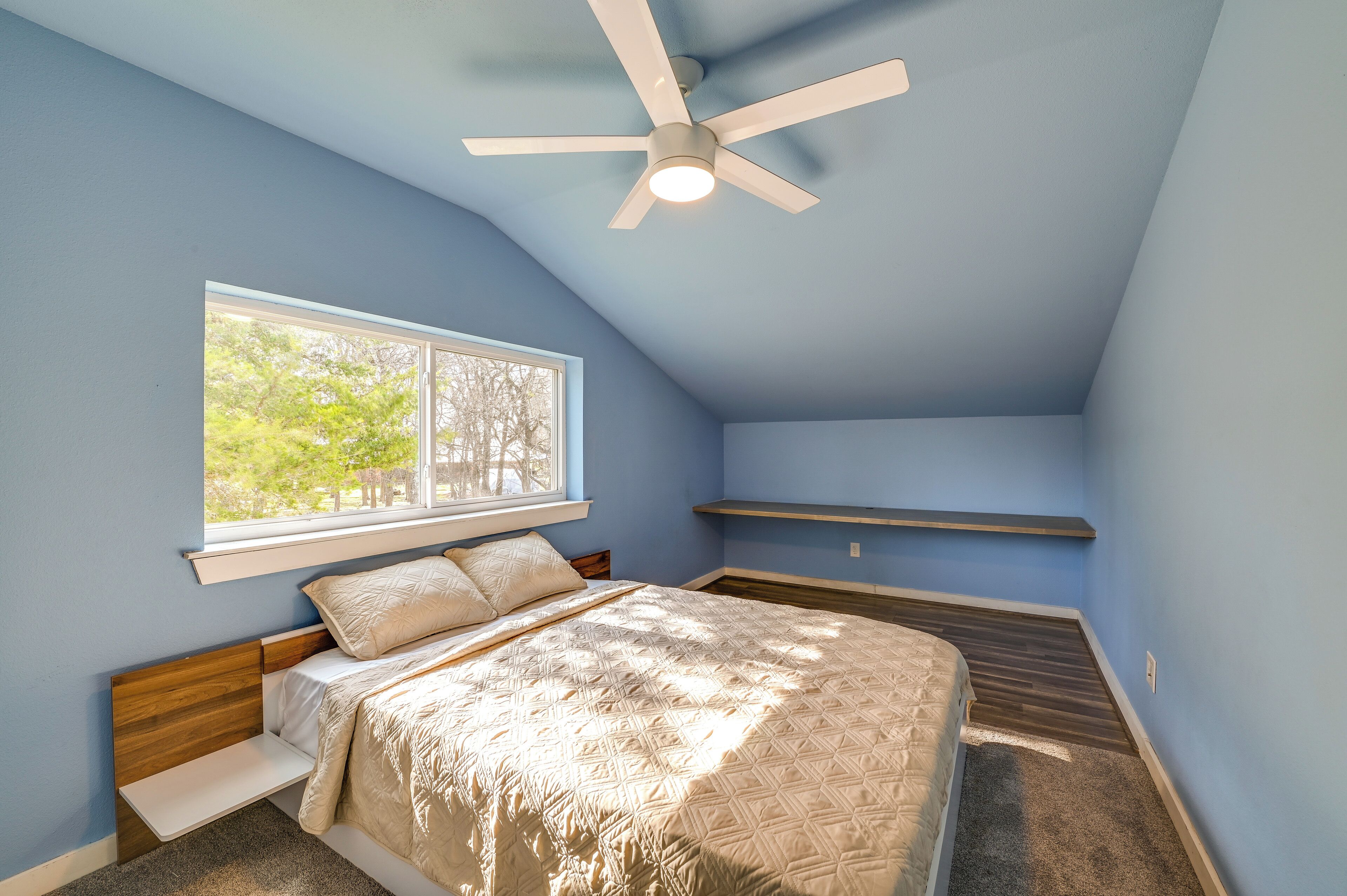 A bedroom with a bed, a ceiling fan, a window, and a built-in shelf.