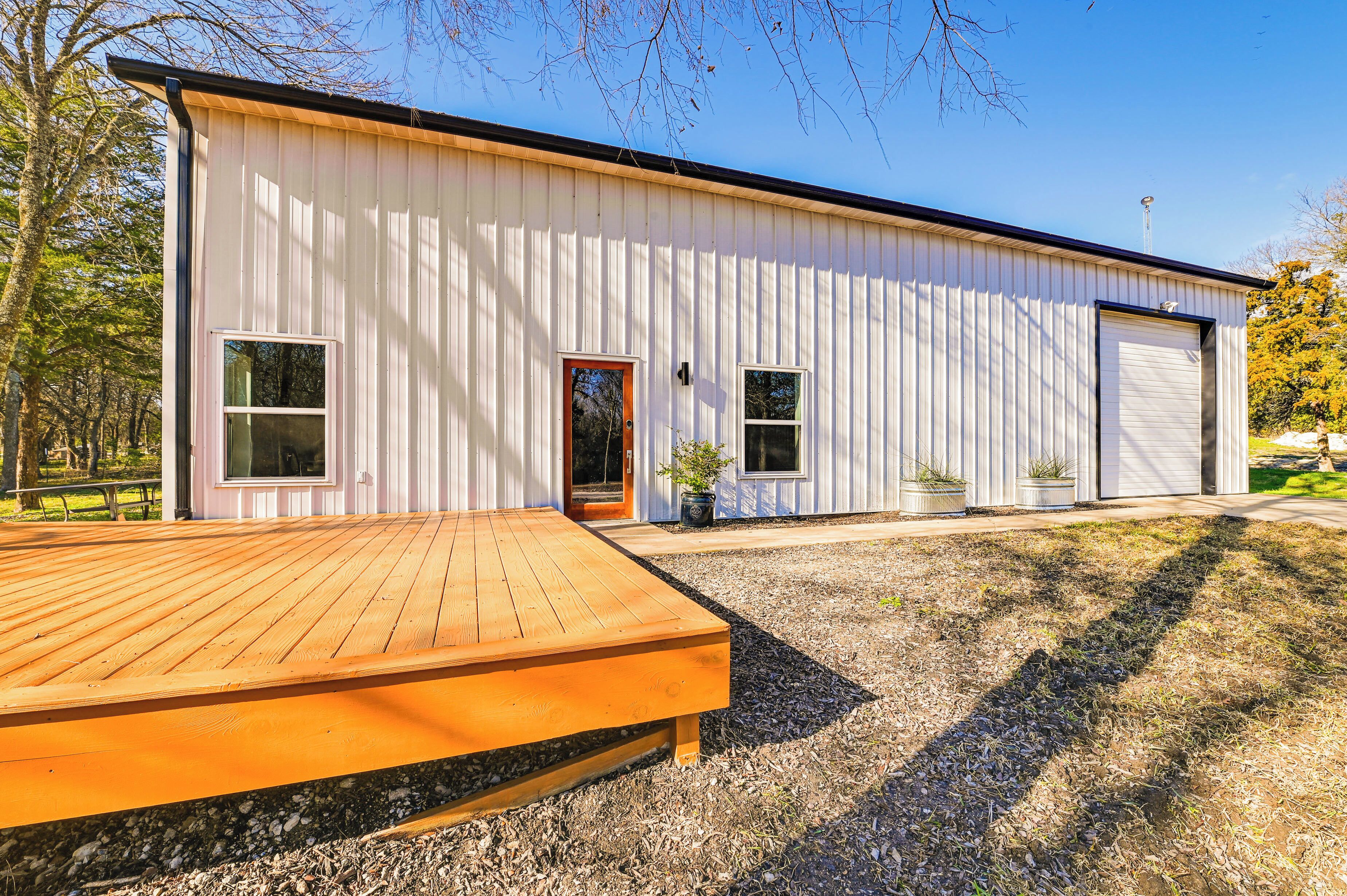 A modern building with a large wooden deck in front, a garage door, and potted plants.
