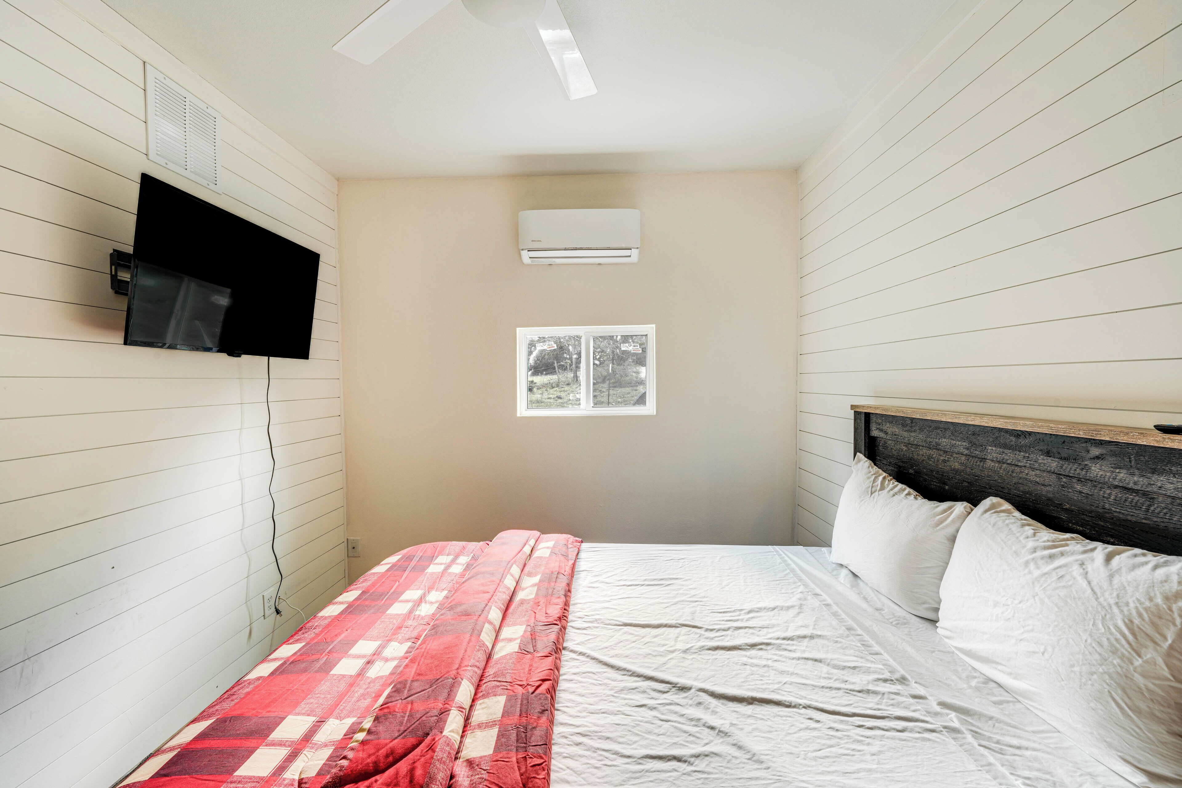 A bedroom with a bed, a mounted TV, an air conditioner, and a window.