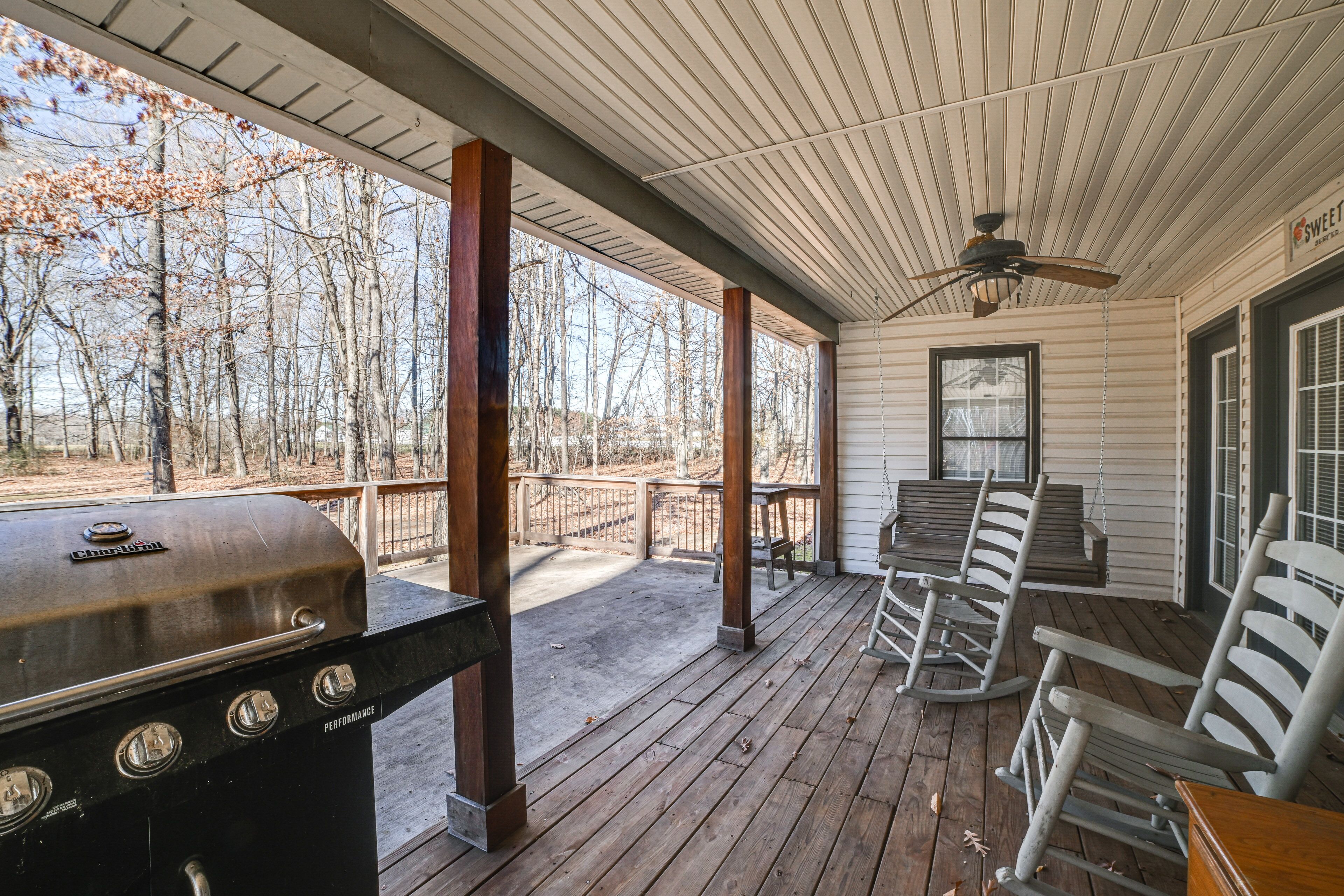 A covered porch with a grill, rocking chairs, and a table.