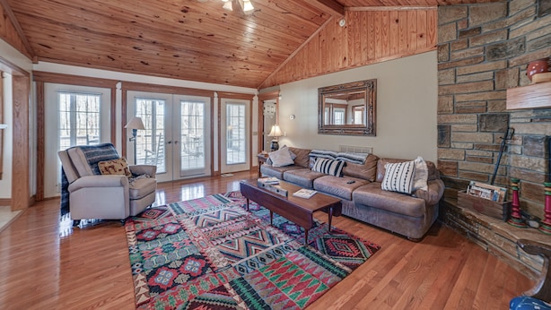 A spacious living room with a wooden ceiling, a stone fireplace, and a large window. - Clarksville Home w/ Porch & Fishing Pond Access! (Clarksville)