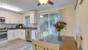 Une cuisine moderne avec des meubles blancs, une table à manger en bois et un ventilateur de plafond.