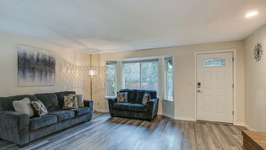Un salon avec un canapé gris, un canapé bleu et une lampe sur pied. On y trouve une porte avec une fenêtre et un objet décoratif accroché au mur.