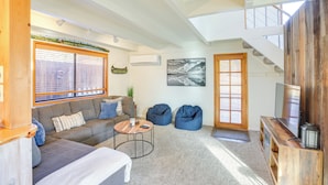 A spacious living room with a sofa, coffee table, and bean bags. There is a TV and a wooden entertainment unit. A staircase is visible in the background. - Bend Home w/ Fire Pit, 4 Mi to High Desert Museum! (Bend)
