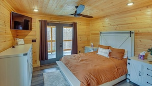 Une chambre dans un chalet en bois, avec un lit, un ventilateur de plafond, une télévision et une porte coulissante donnant sur l’extérieur.