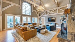 A spacious living room with a large sectional sofa, a coffee table, and a fireplace. There is a large window providing natural light and a view of the outdoors. - Monterey Home w/ Hot Tub, Pool & Game Room! (Monterey)