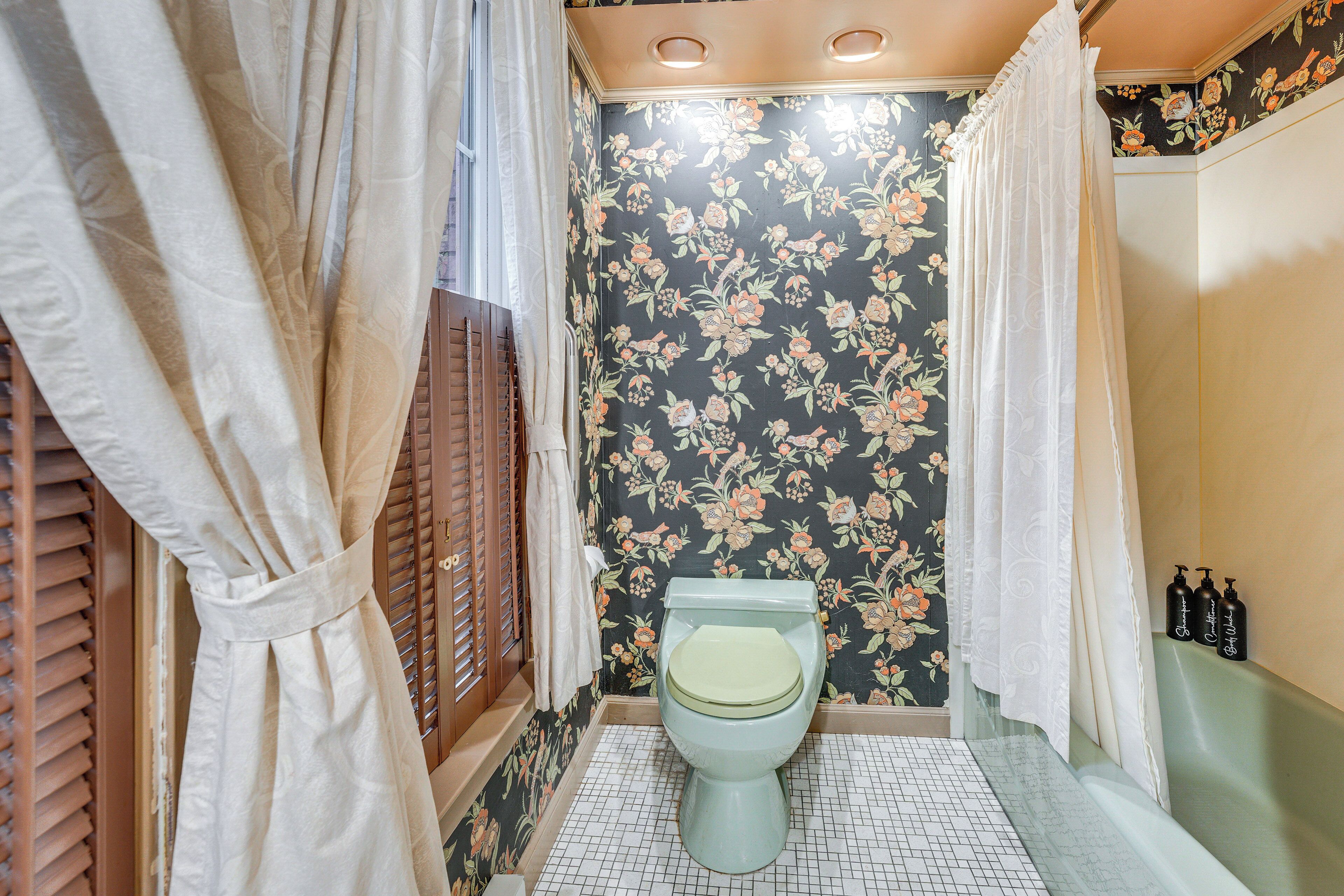 A bathroom with a floral wallpaper, a toilet, and a shower curtain.
