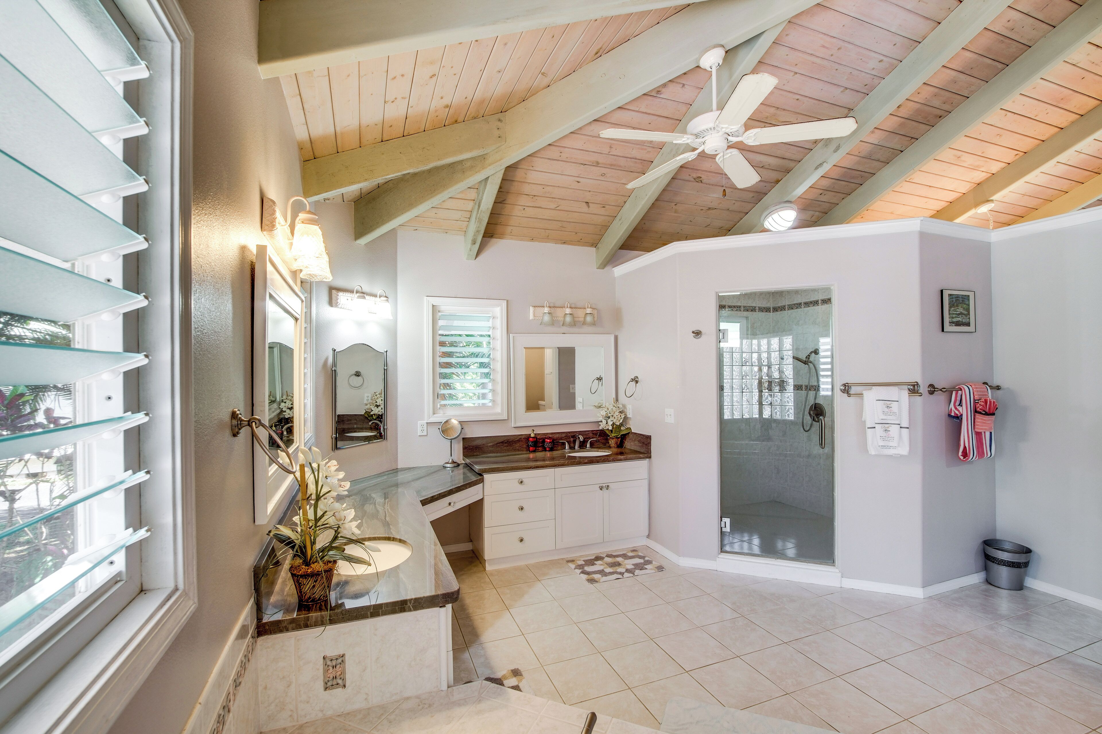 A bathroom with a glass shower enclosure, a vanity with a sink, and a ceiling fan.
