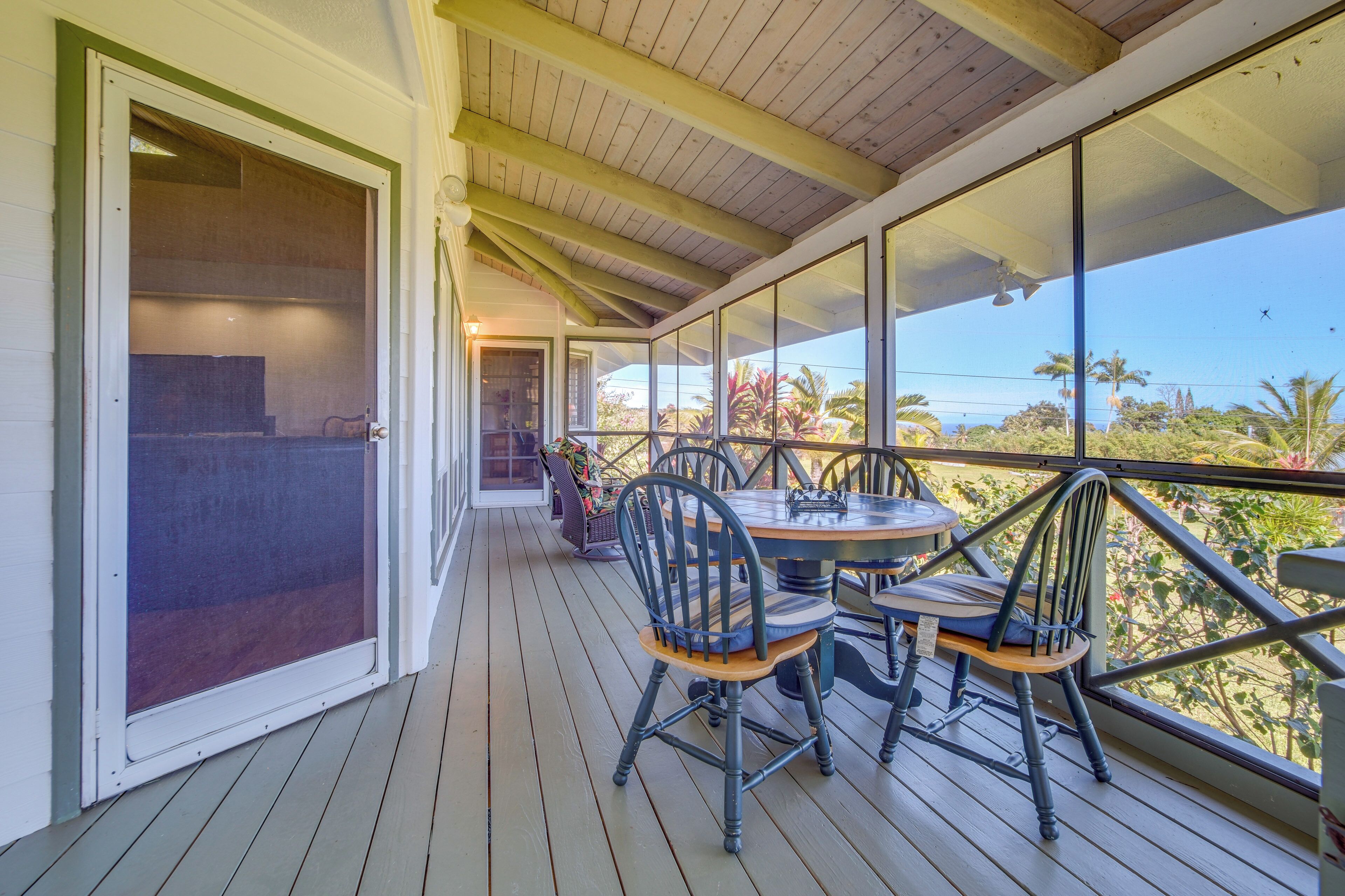 A covered outdoor area with a table and chairs, a sliding glass door, and a view of palm trees.