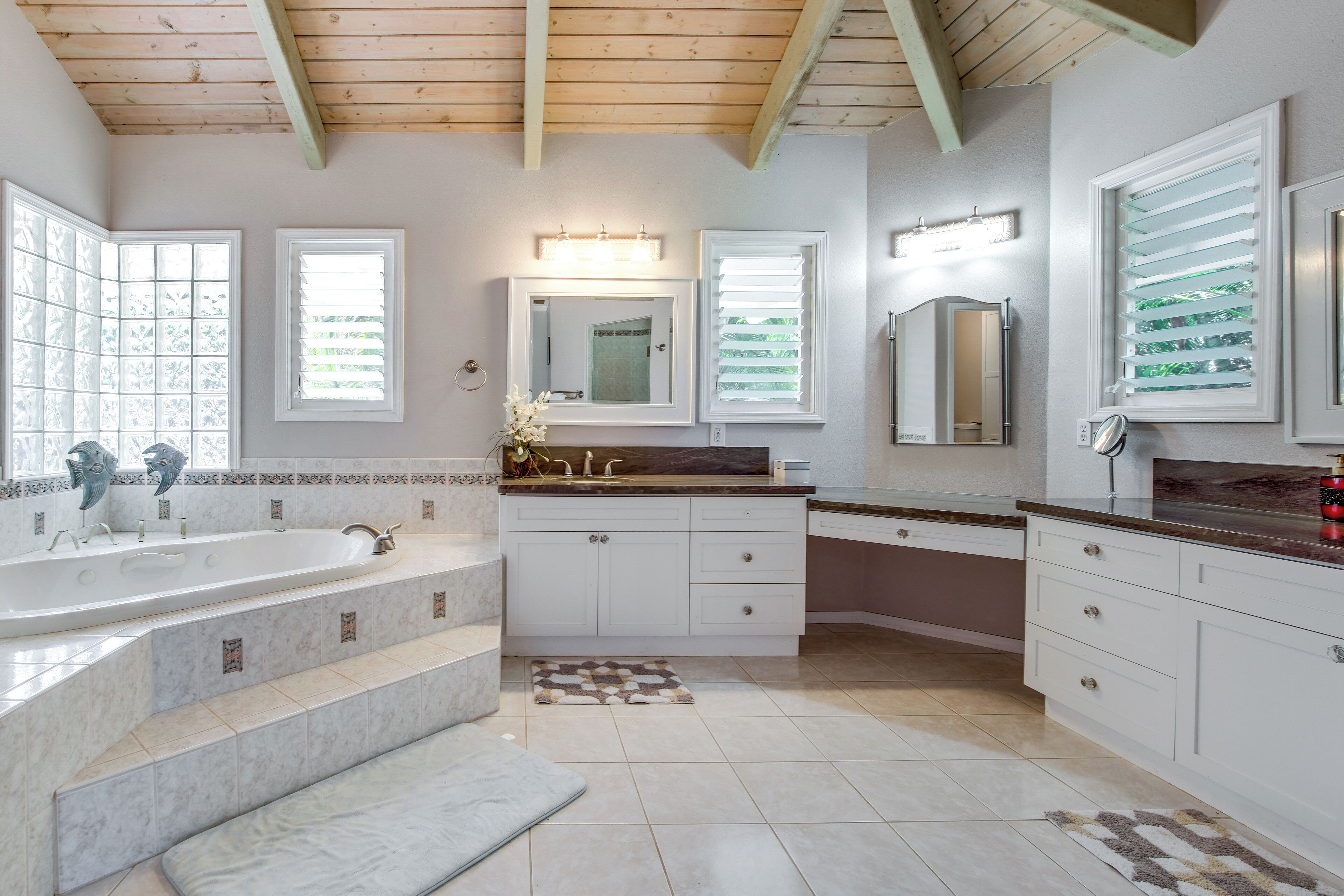 A spacious bathroom with a large bathtub, a vanity with a mirror, and a window with blinds.