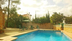 A swimming pool with a curved edge, surrounded by a stone wall and a wooden fence. - Vista al Mar, Piscina y Paz: tu Escape Perfecto en Esta Casa Rural Única (Sant Miquel)
