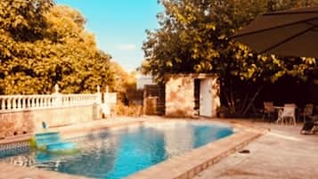 A swimming pool with a stone border, surrounded by trees and a covered patio area.