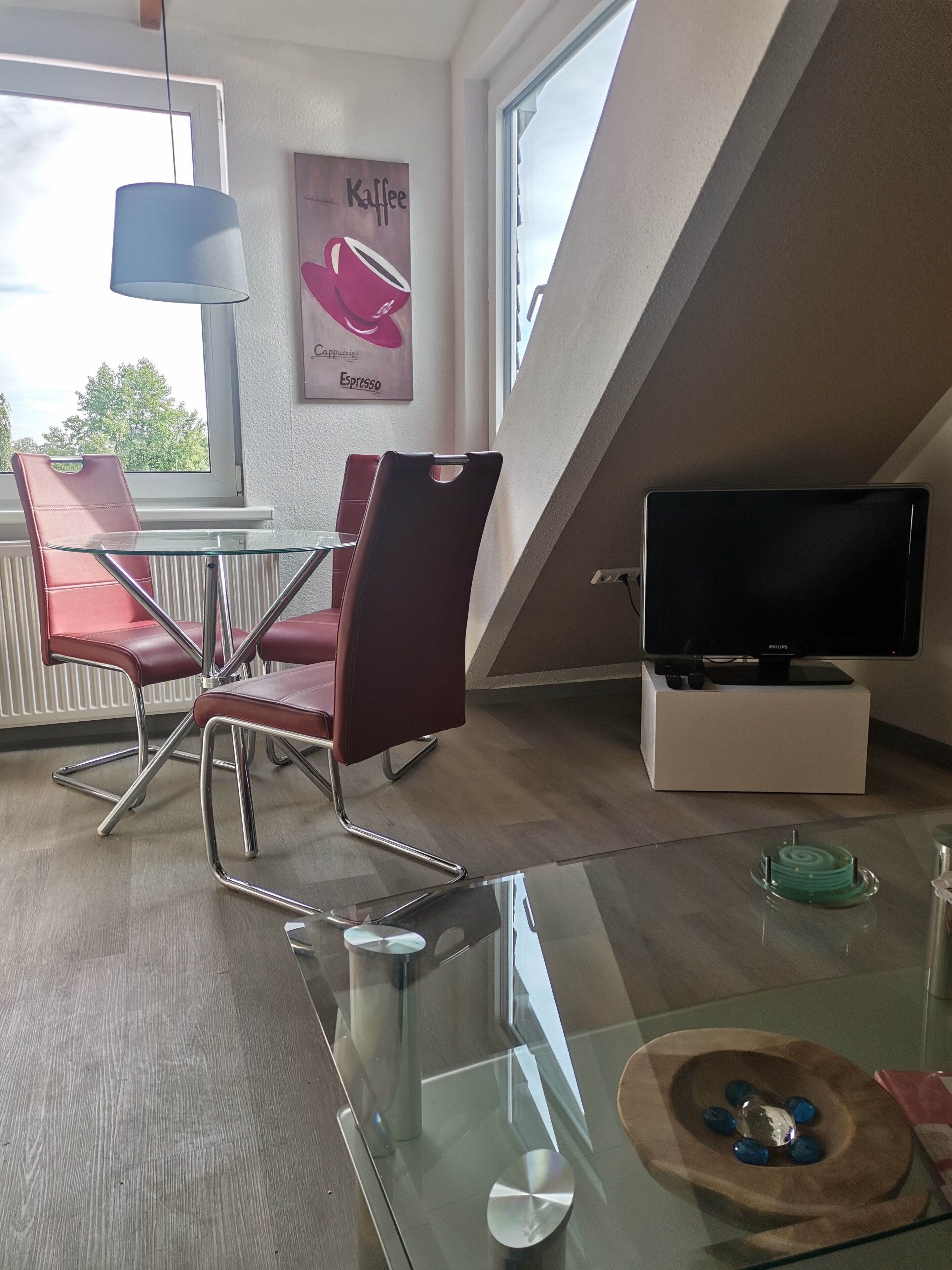 En moderne stue med et glasbord, røde stole, et fladskærms-tv og vægkunst med kaffemotiver.