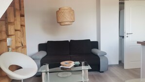 Un soggiorno moderno con un tavolino in vetro, un divano nero con cuscini grigi, una poltrona bianca e una lampada a sospensione intrecciata.