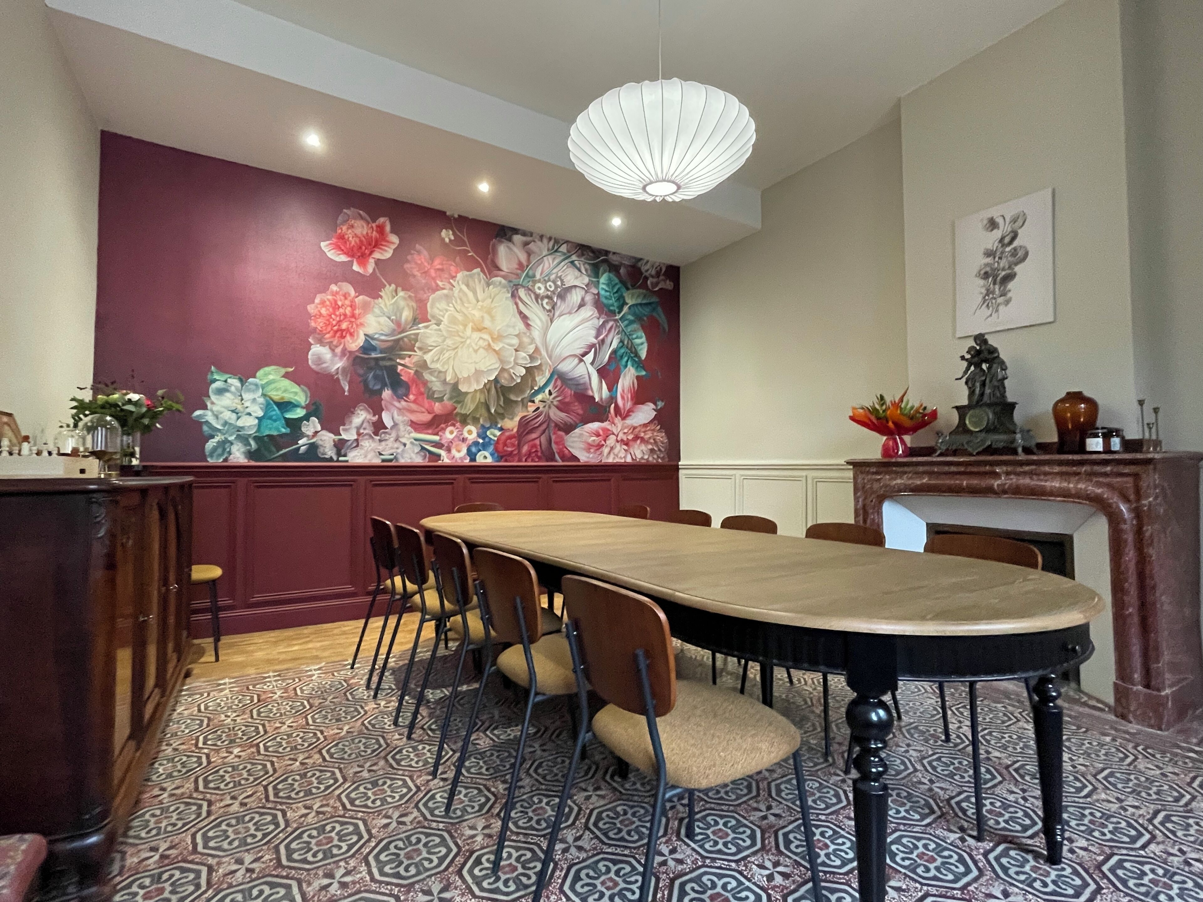 A dining area with a large floral mural, a wooden table, and patterned floor tiles.