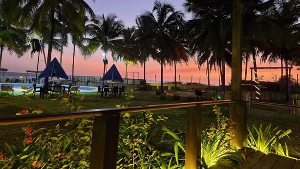 A beachside resort with palm trees, outdoor seating, and a view of the ocean at sunset. - Bamboo Beach Resort (Monrovia)