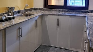 A kitchen with white cabinets, a marble countertop, and a window with a view of palm trees. - Bamboo Beach Resort (Monrovia)