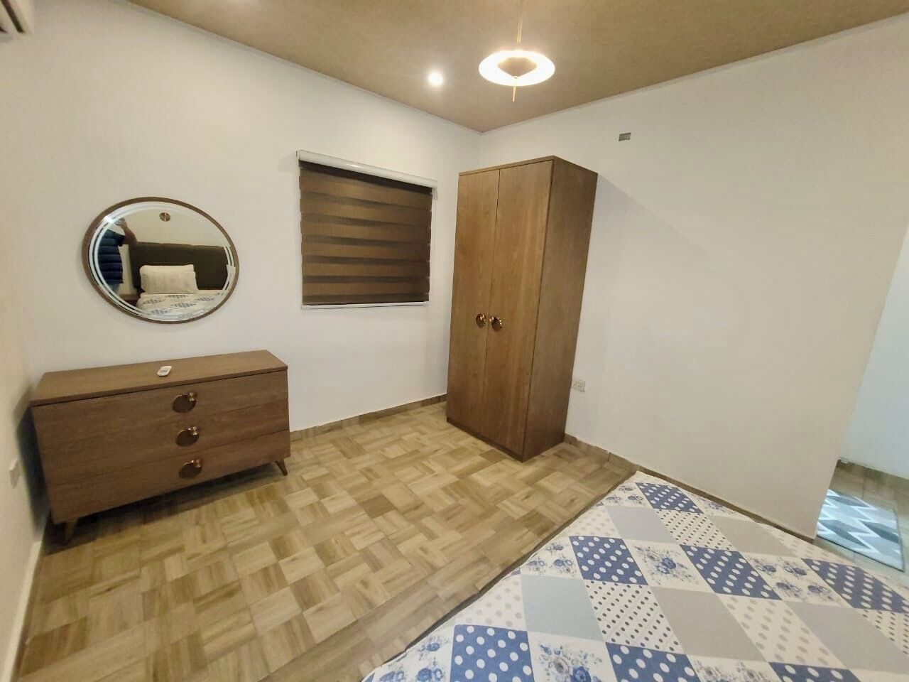 A bedroom with a wooden wardrobe, a dresser, a mirror, and a patterned rug.