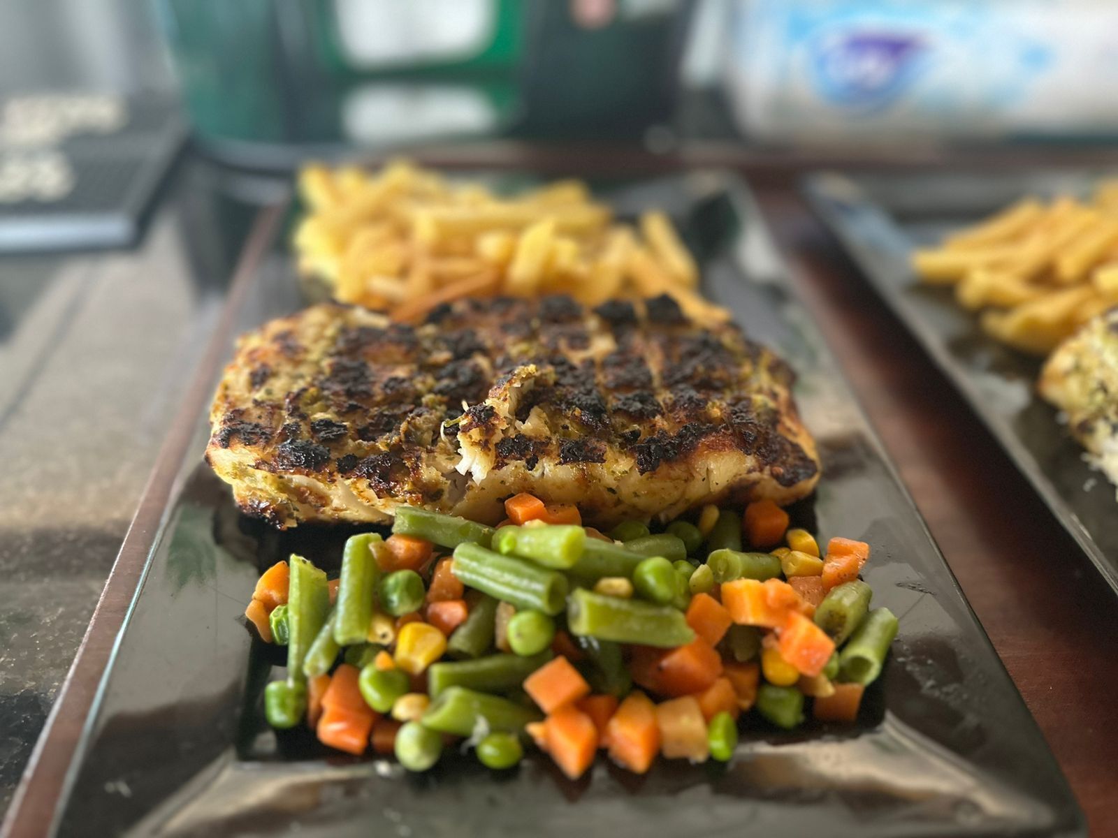 Une assiette contenant du poulet grillé, des haricots verts et des carottes.