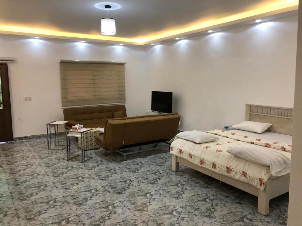 A bedroom with a bed, a sofa, a TV, and a small table.