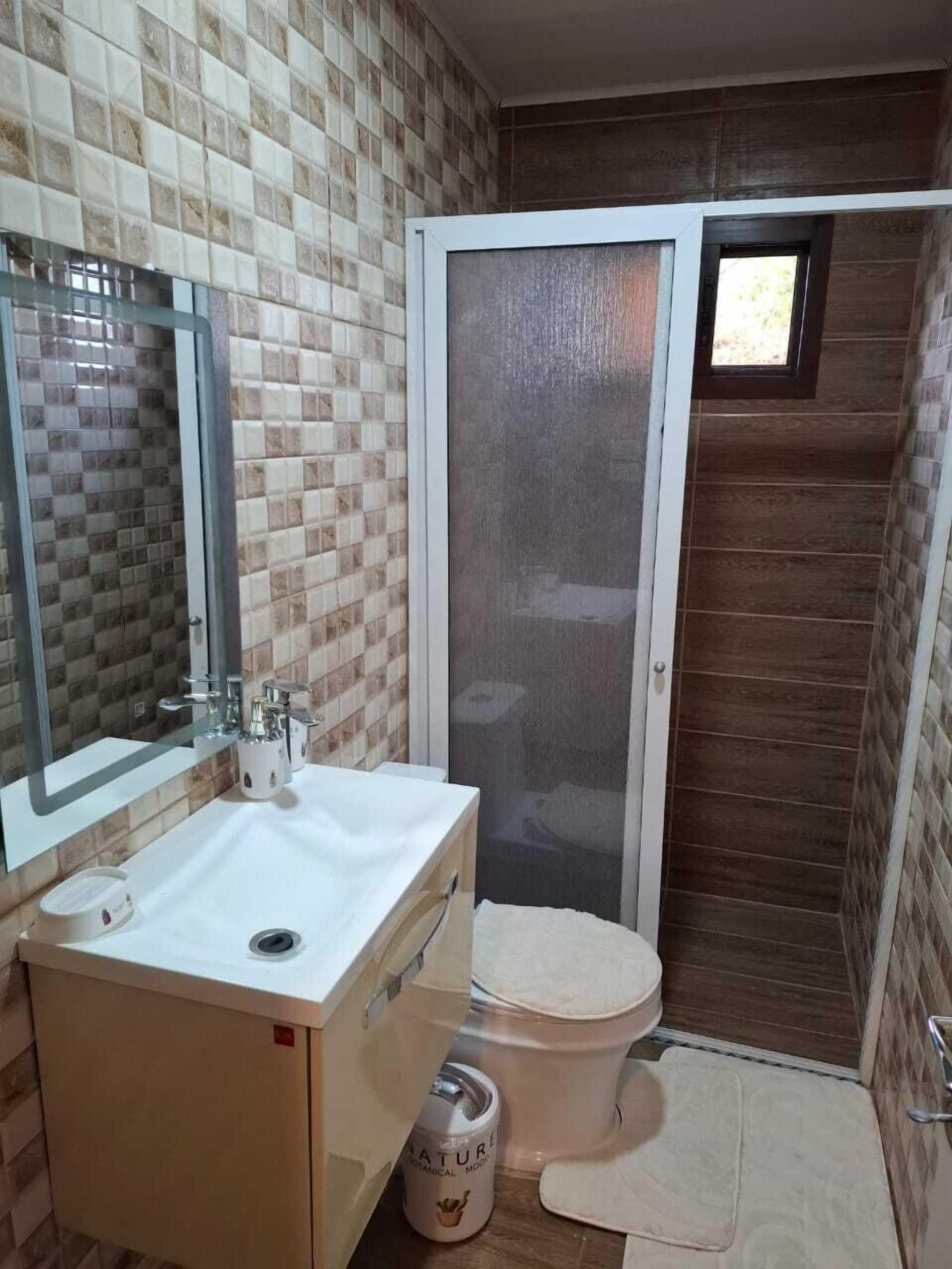 Un baño con pared de azulejos, un lavamanos con espejo, un inodoro y una cabina de ducha.