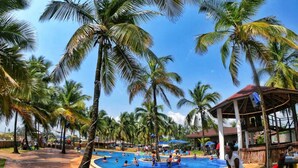 A pool area surrounded by palm trees, with a covered seating area and a building in the background. - Bamboo Beach Resort (Monrovia)