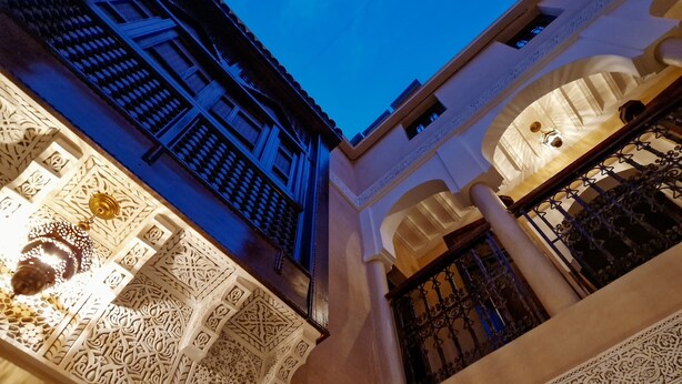 An interior courtyard with intricate white architectural details, columns, and a decorative ceiling light fixture. - Click Riad & Spa (Marrakech)