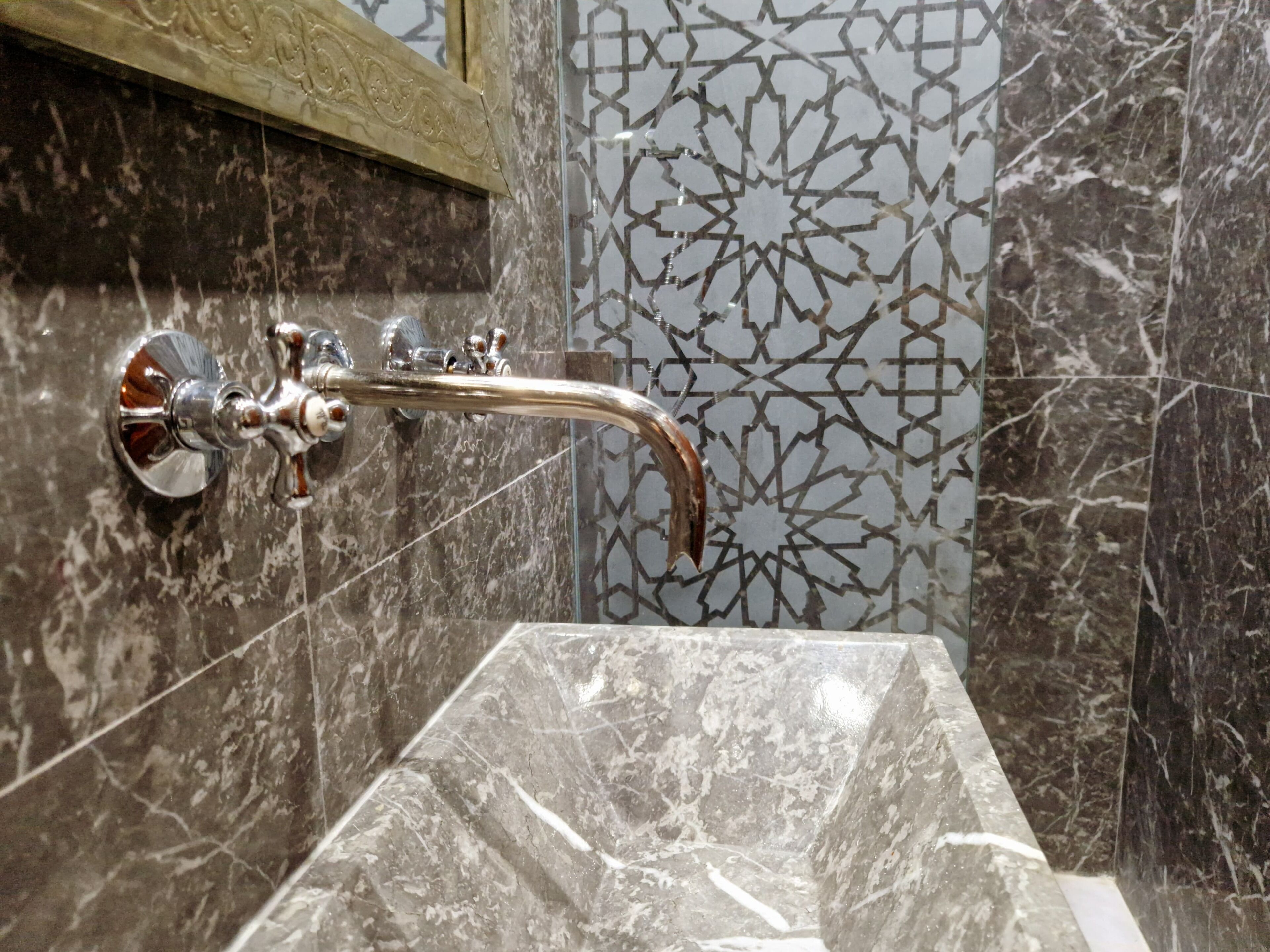 Une salle de bain avec un lavabo en marbre, un robinet chromé et des carreaux décoratifs sur les murs.