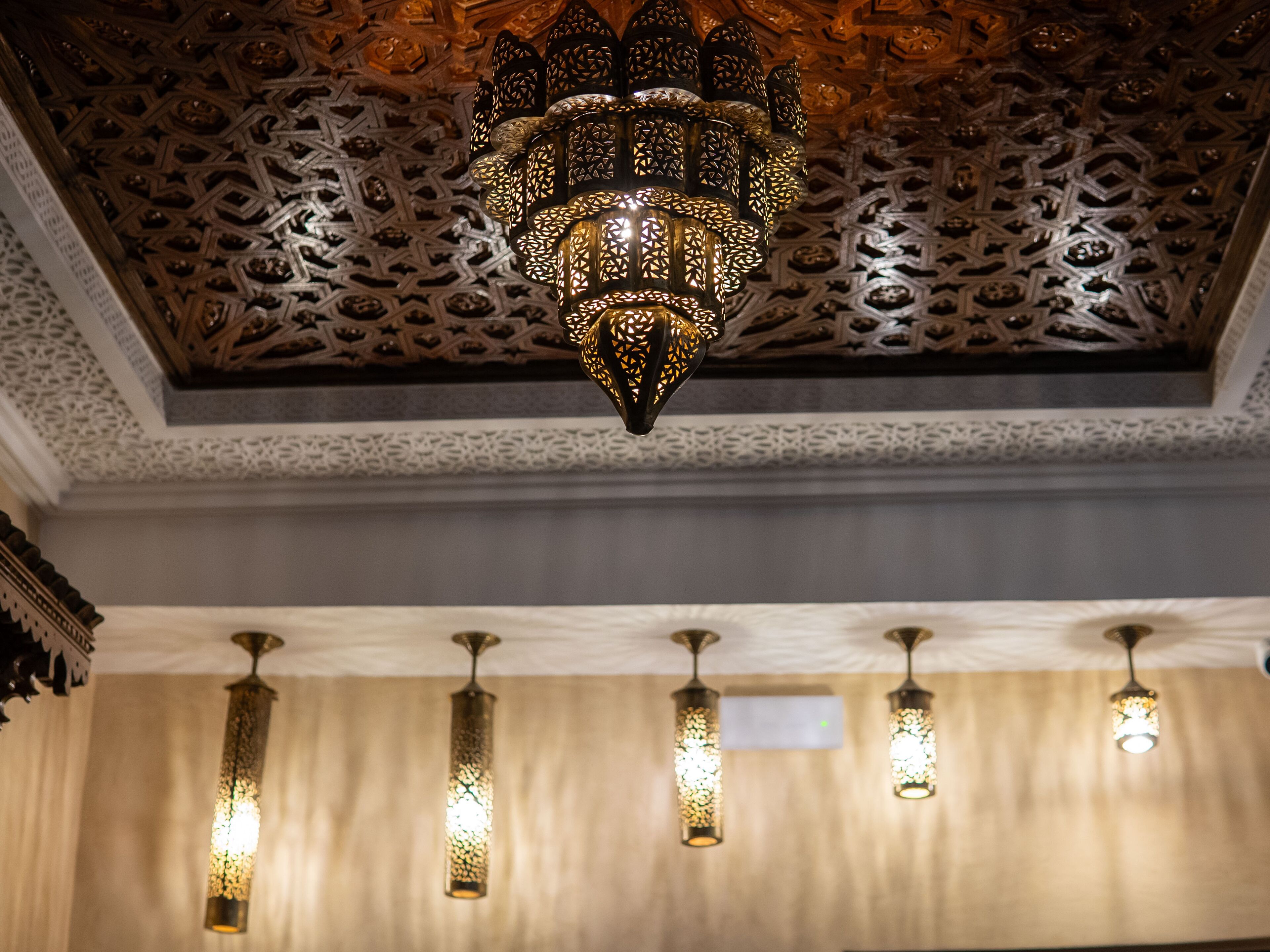 A chandelier with intricate metalwork and a patterned ceiling.