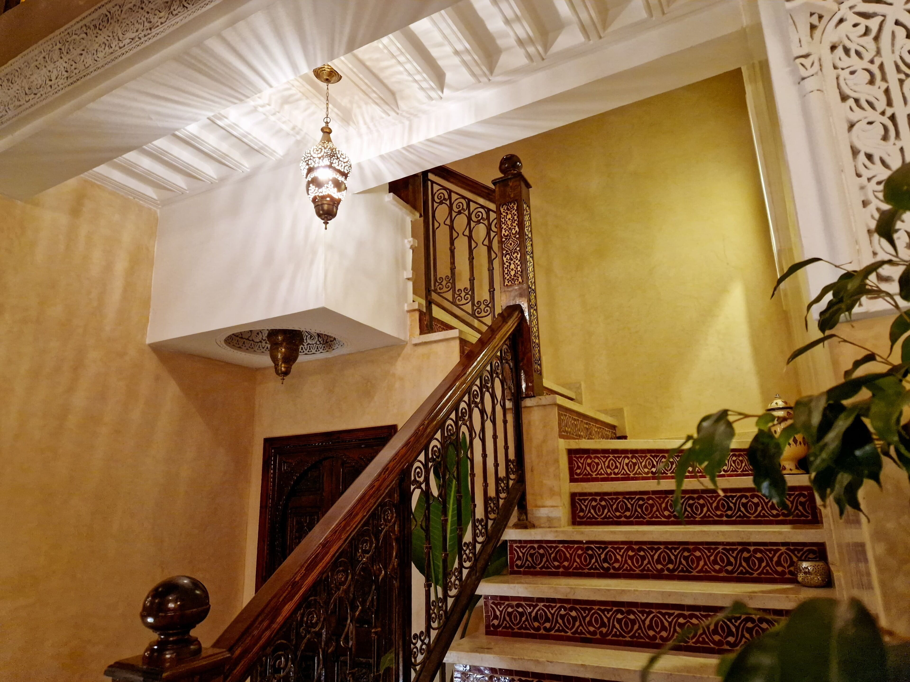 Un magnifique escalier orné de balustrades travaillées et surmonté d’un lustre.