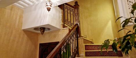 Un magnifique escalier orné de balustrades travaillées et surmonté d’un lustre.