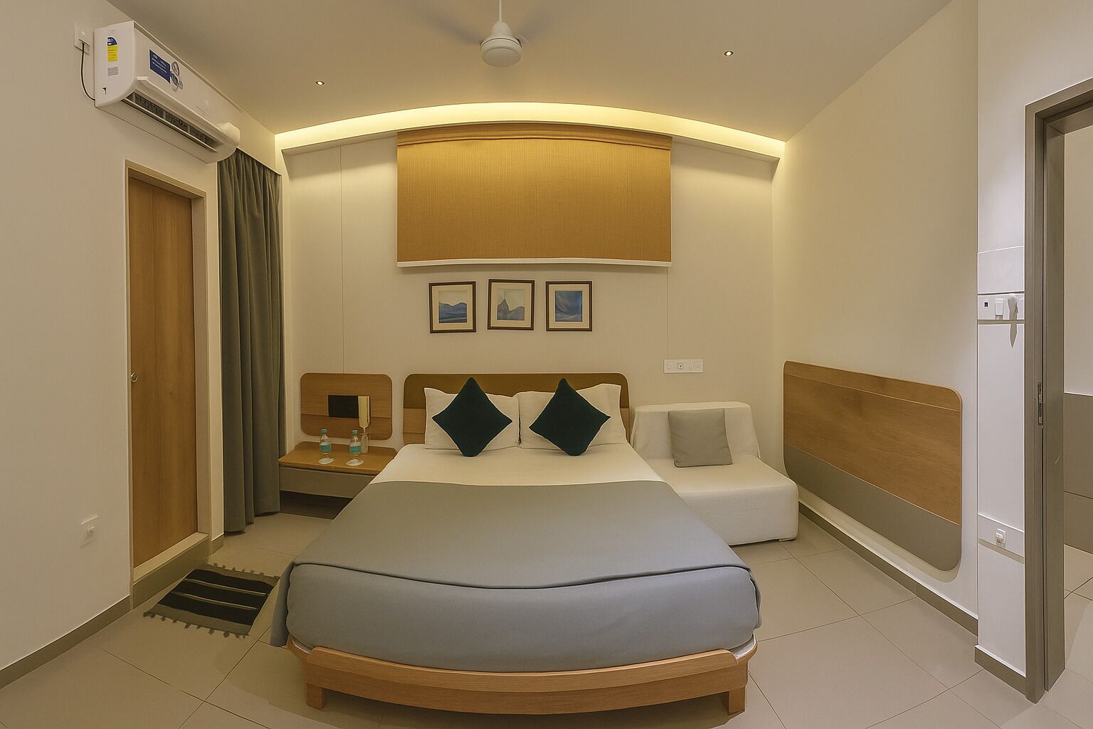 A hotel room with a large bed, bedside tables, a bedside lamp, a wall-mounted air conditioner, and a ceiling fan.