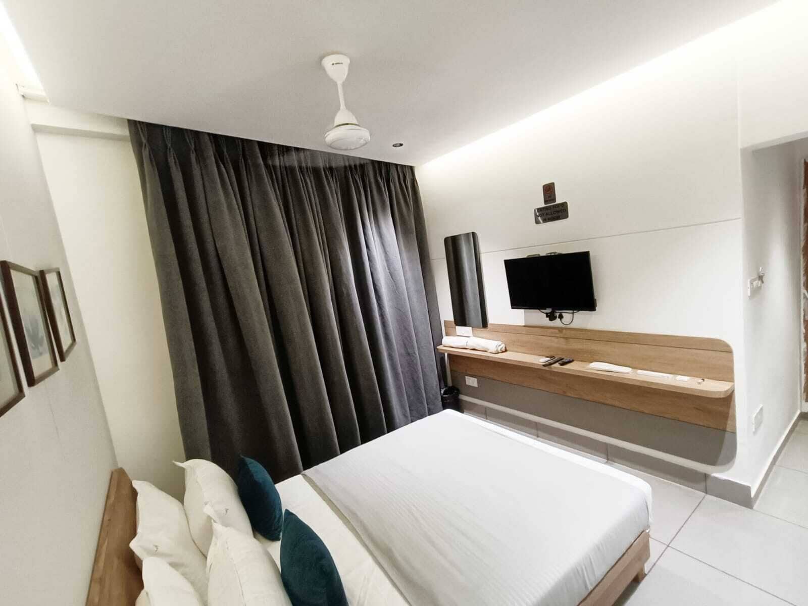 A modern hotel room with a large bed, a flat-screen TV, a wooden bedside table, and a ceiling fan.