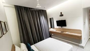 A modern hotel room with a large bed, a flat-screen TV, a wooden bedside table, and a ceiling fan.