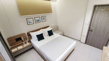A hotel room with a bed, bedside tables, a nightstand, a wooden headboard, a door, and a wall-mounted light fixture.