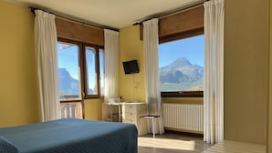 Habitación de hotel con cama, escritorio, silla y un amplio ventanal con vistas a la montaña.