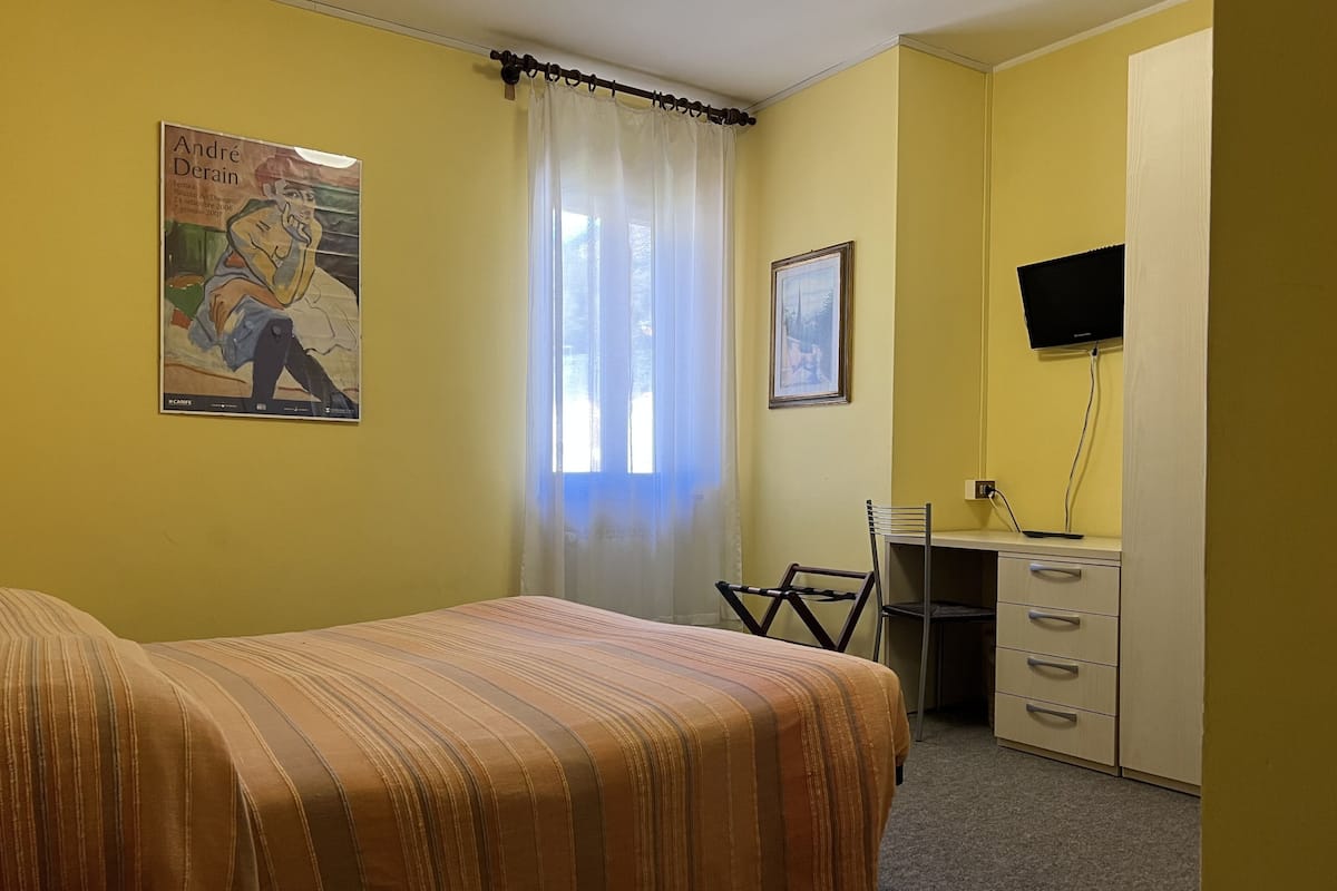 Una habitación con cama, escritorio, silla, televisor y un cartel en la pared.