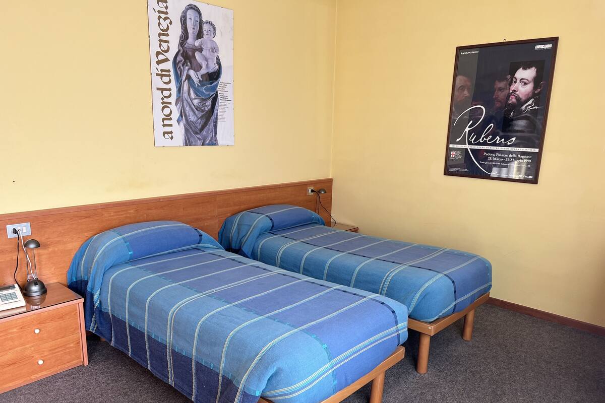 Una habitación con dos camas, cabecera de madera, mesita de noche y lámpara.