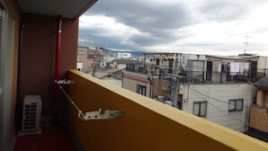 Un balcon doté d’une rambarde jaune, donnant sur un quartier résidentiel composé de plusieurs immeubles, sous un ciel nuageux.