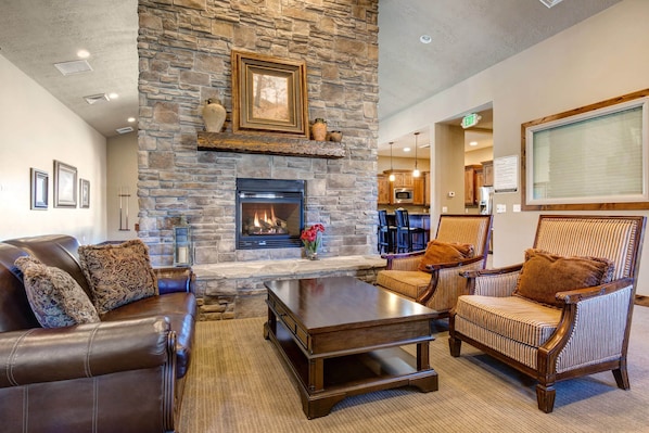 A cozy living area with a stone fireplace, leather sofa, striped armchairs, and a coffee table.