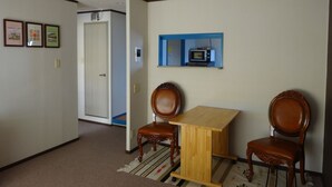 A room with a wooden table and two chairs, a door, and a wall-mounted shelf with a microwave. - It has a kitchen, closet, shoe closet, washing machine, balcony and parking space. Clothes can be dried on the balcony, or room-dried. The 46 sq. m. of space is ideal for long-term stays. (大阪市)