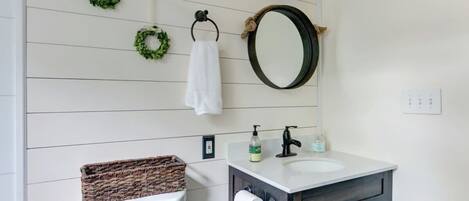 Een badkamer met een wit toilet, een donker houten wastafelmeubel, een ronde spiegel en twee groene kransen aan de muur.