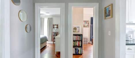 A hallway with wooden flooring, white walls, and a bookshelf with books.