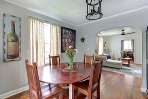 A dining area with a round wooden table, chairs, a vase of flowers, and a painting of a wine bottle. - Shades of Blue on Park - Walk to Forsyth! (Savannah)