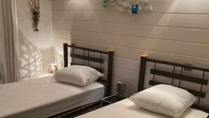 Una habitación con dos camas individuales, cada una con estructura de madera y ropa de cama blanca. Hay luces fijadas a la pared y un objeto decorativo sobre las camas.